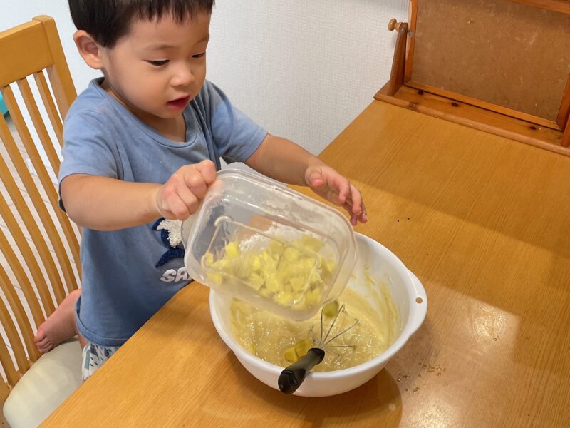 蒸しパンの材料にカットしたさつまいもを入れる子ども