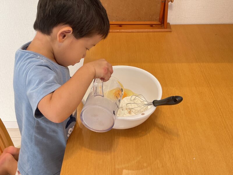 さつまいもの蒸しパンの材料を入れる子ども