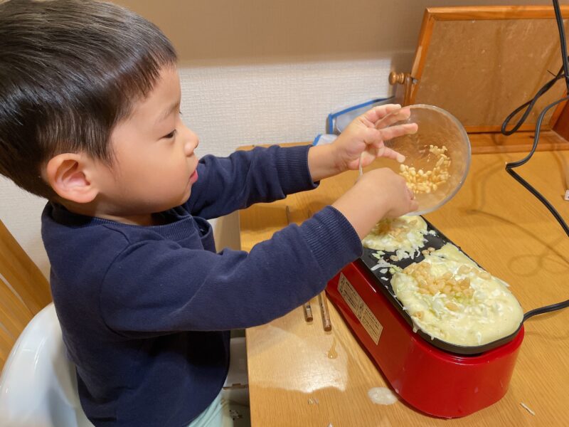 メガたこ焼き器に天かすを入れる子ども