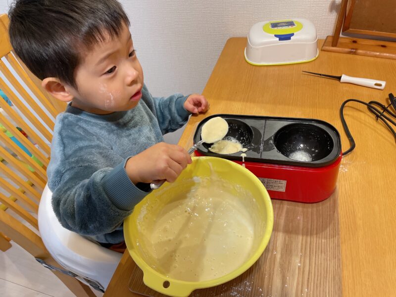 メガたこ焼き器にホットケーキの材料を入れる子ども