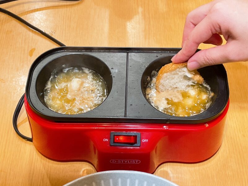 メガたこ焼き器で作ったアヒージョにバケットをつけている