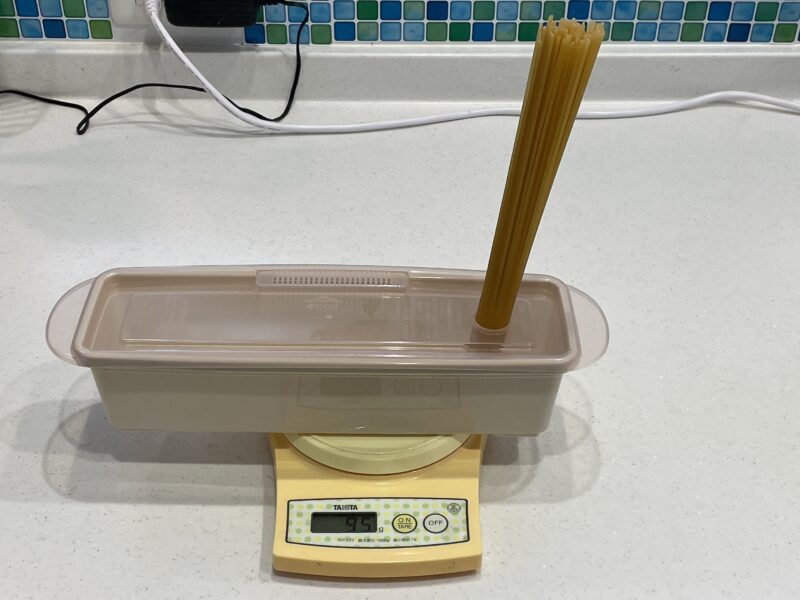 電子レンジ調理容器にパスタを入れて重さを量っている